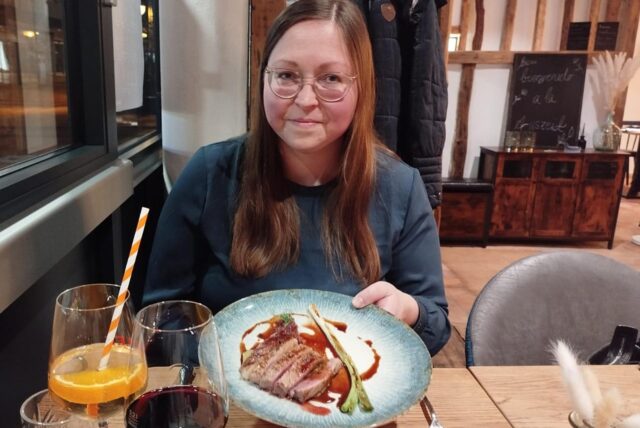 Eine Frau hält einen Teller mit Fleisch in die Kamera