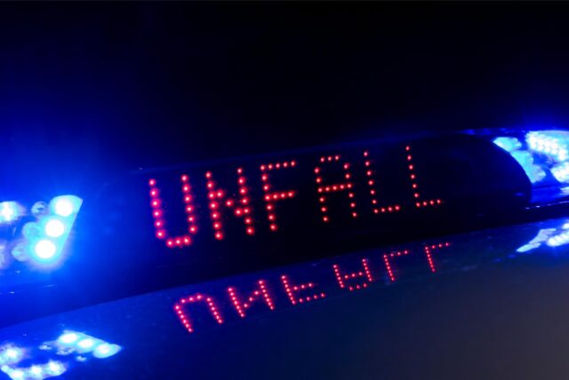 Das Blaulicht auf einem Fahrzeug der Polizei leuchtet in der Dunkelheit, während auf dem Display der Hinweis «Unfall» zu lesen ist. (Symbolbild)