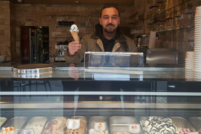 Inhaber Adim Ulupinar hält hinter der Eistheke des Café Laren in Marl-Hüls eine Waffel mit einer Kugel Eis in der Hand.