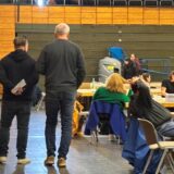 Bundestagswahl 2025 in Castrop-Rauxel: In der Europahalle werden die Stimmzettel aus der Briefwahl gezählt. Zwei Männer schlendern zwischen den Tischen hindurch und beobachten die Vorgänge.