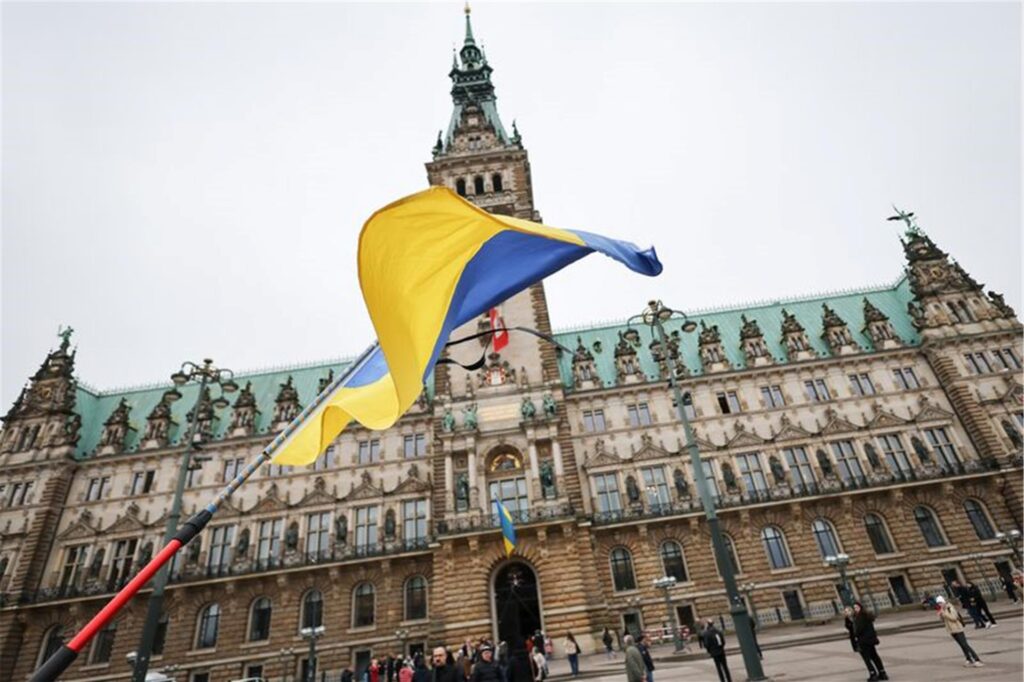 Ein Mann steht mit ukrainischer Fahne und Trauerfloor bei der Gedenkminute „Hamburg steht still“ vor dem Rathaus. Ein Mann steht mit ukrainischer Fahne und Trauerfloor bei der Gedenkminute „Hamburg steht still“ vor dem Rathaus.
