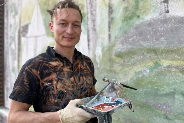 Künstler Juri Schäffer steht vor seinem Kunstwerk an der Wilhelm-Lehmbruck-Schule in Deuten.