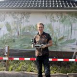 Künstler Juri Schäffer steht mit seinen Mal-Utensilien in der Hand vor seiner gestalteten Wand an der Grundschule in Deuten.