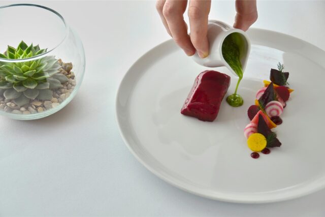 Eine Hand schüttet grüne Sauce auf einen Haute-Cuisine-Teller.