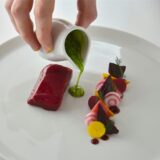Eine Hand schüttet grüne Sauce auf einen Haute-Cuisine-Teller.
