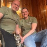 Lars Riedel und Christina Oddey sitzen im Flur auf dem Boden gemeinsam mit Bandit