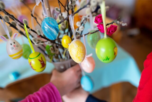 Zwei Kinder halten einen Palmbuschen mit bemalten Ostereiern in den Händen.