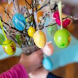 Zwei Kinder halten einen Palmbuschen mit bemalten Ostereiern in den Händen.