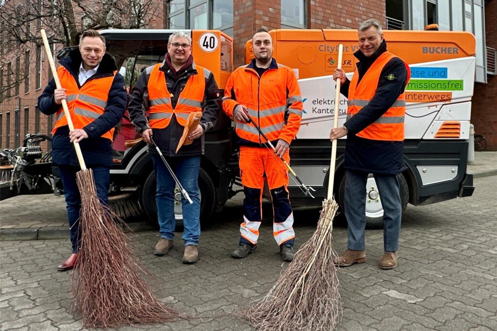 Bürgermeister Christoph Tesche, KSR-Mitarbeiter Manuel Kieper, KSR-Abfallberater Matthias Berger und KSR-Betriebsleiter Roland Wrobel halten Besen und Greifzangen in den Händen und stehen vor einem Fahrzeug der KSR Recklinghausen