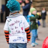 Kinder spielen, eins trägt ein T-Shirt mit der Aufschrift „Ich möchte in die Kita“.