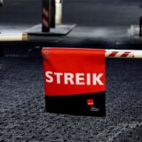 Eine Schranke ist geschlossen, daran hängt ein Plakat auf dem steht „Streik“
