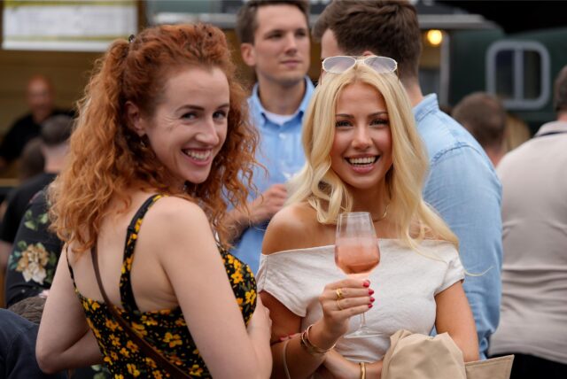 Zwei Frauen lächeln auf dem Feierabendmarkt in Dortmund mit einem Getränk in der Hand in die Kamera.