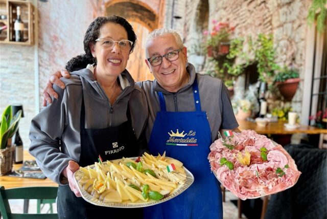 Zwei Personen präsentieren jeweils eine Platte mit Speisen. Eine Person hält eine Platte mit Wurstwaren und die andere eine Platte mit Käse.