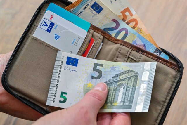 Eine Frau hält in ihrer Hand eine Brieftasche mit Geld und Bankkarten.