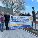 Sieben Personen stehen vor der Stadthalle Dattelns und halten ein Plakat mit der Aufschrift After Job Party hoch.