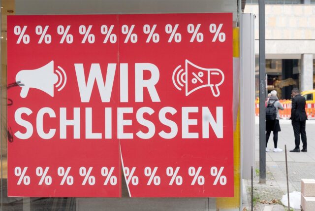 Am Schaufenster eines Geschäftes hängt ein Schild mit der Aufschrift. „Wir schließen“.