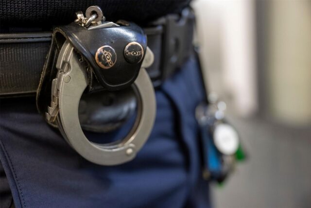 Eine Handschelle hängt am Gürtel eines Polizisten.