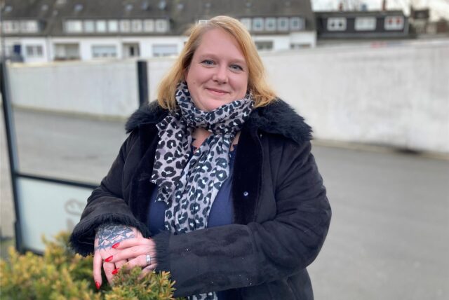 Ein Porträt von Yvonne Steinmüller, die in Herten-Westerholt an einer Hecke steht, auf der sie beide Hände angelegt hat.