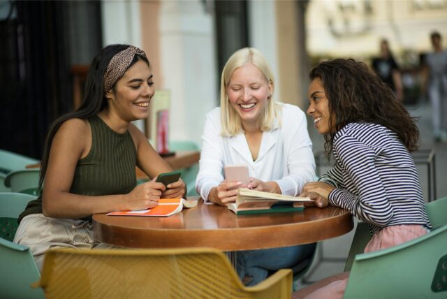 Drei Frauen sitzen am Tisch und gucken auf ihre Smartphones.