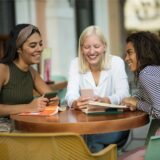 Drei Frauen sitzen am Tisch und gucken auf ihre Smartphones.