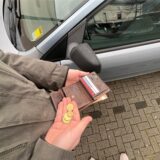 Ein Mann steht neben einem Auto, hält seine Geldbörse in der linken Hand und einige Münzen in der anderen. (Symbolbild)