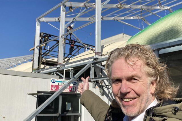Centermanager Olaf Magnusson steht auf einem Parkdeck und zeigt auf die Baustelle auf dem Dach des Einkaufszentrums. Im Hintergrund angeseilte Arbeiter, die an einem Gerüst bauen.