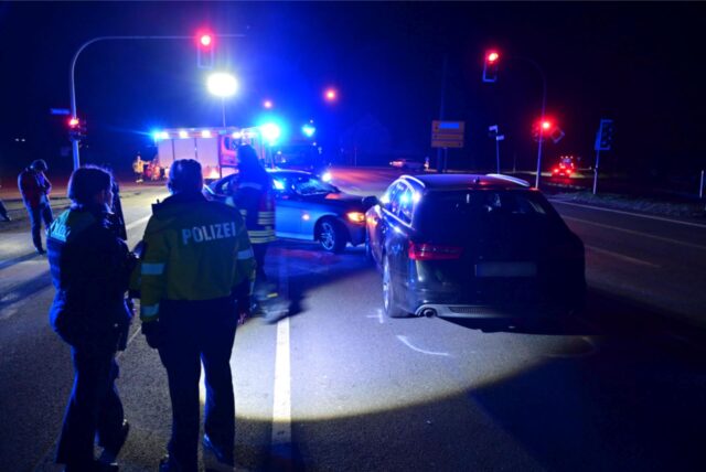 Polizisten stehen an einer Unfallstelle mit zwei zusammengestoßenen Wagen.