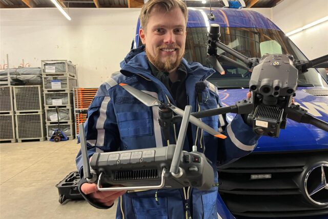 Thomas Lütkenhaus hält vor einem THW-Fahrzeug eine Drohne mit Fernbedienung in die Kamera.