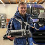 Thomas Lütkenhaus hält vor einem THW-Fahrzeug eine Drohne mit Fernbedienung in die Kamera.