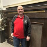 Ein Mann in rotem Poloshirt und schwarzem Swaeter steht vor einer Wand im Sitzungssaal des Rathauses in Datteln.