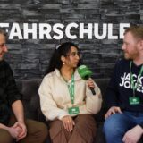 Fahrlehrer Sebahattin Altunsoy sowie Rosi Taslima Azam und Jonas Alder von der Hertener Allgemeinen sitzen bei einem Interview auf einem Sofa, im Hintergund ist „Fahrschule“ zu lesen.