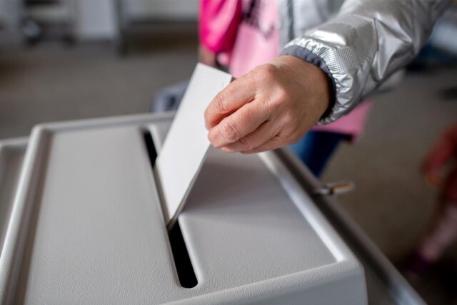 Eine Person wirft einen Stimmzettel in eine Wahlurne.
