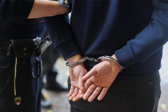 Mann in Handschellen wird von Polizei abgeführt.