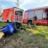Einsatzfahrzeuge von Feuerwehr und Rettungsdienst stehen am Rand einer Straße, im Graben liegt ein blaues Motorrad. Zwei Polizisten stehen neben dem Graben.