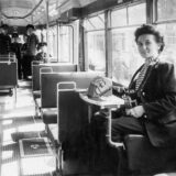 Das historische Foto einer Schaffnerin, die in einem Straßenbahnwagen sitzt.