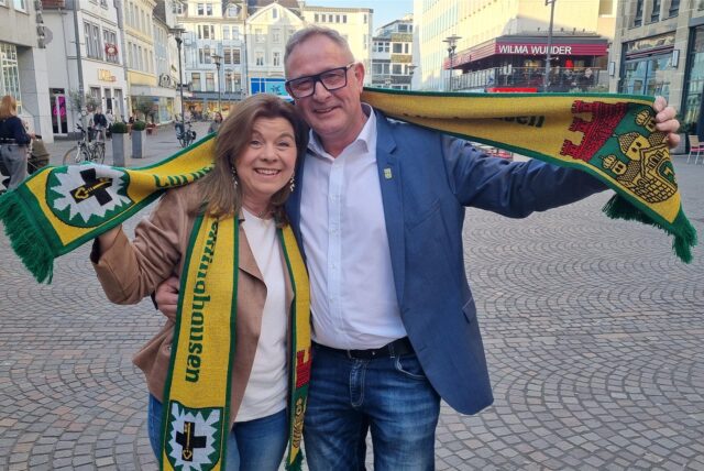 Das neue Stadtprinzenpaar, Veronika Eberhardt und Rainer Herzog, stehen mit Vereinsschal auf dem Altstadtmarkt in Recklinghausen.