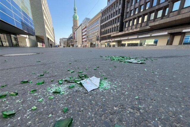 Scherben einer grünen Bierflasche liegen auf einer Straße.