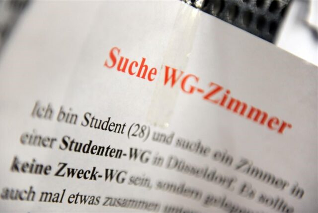 Ein Zettel mit der Aufschrift „Suche WG-Zimmer“ hängt an einem Schwarzen Brett in der Universität in Düsseldorf. (Archivbild)