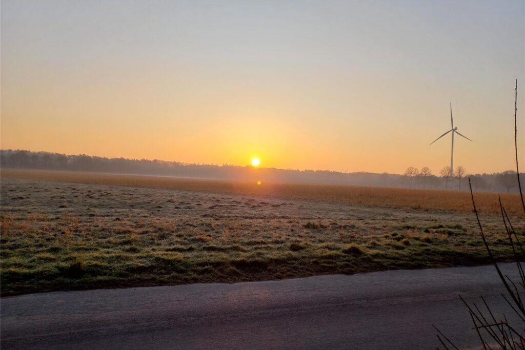 Sonnenaufgang über einer Wiese mit einem Windrad und leichtem Nebel im März 2025 in Haltern.