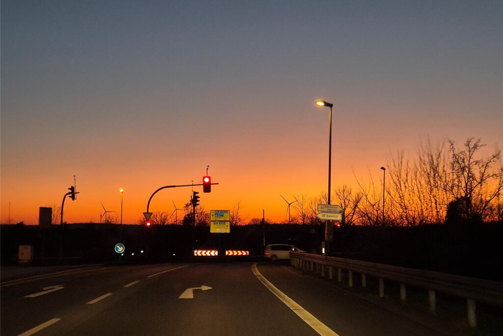 Starke Dämmerung nach Sonnenuntergang im März 2025 ohne Wolken in Haltern am See mit Blick auf rote Ampel und Straße an einer Kreuzung