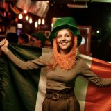Eine Frau steht am St. Patrick’s Day in einer Bar und hält eine irische Flagge hoch.