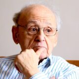 Rolf Abrahamsohn sitzt mit verschränkten Armen auf einem Stuhl und blickt in die Ferne.