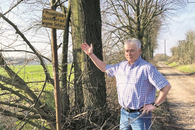 Ein Mann weist an einer Allee auf das Schild Privateigentum hin.