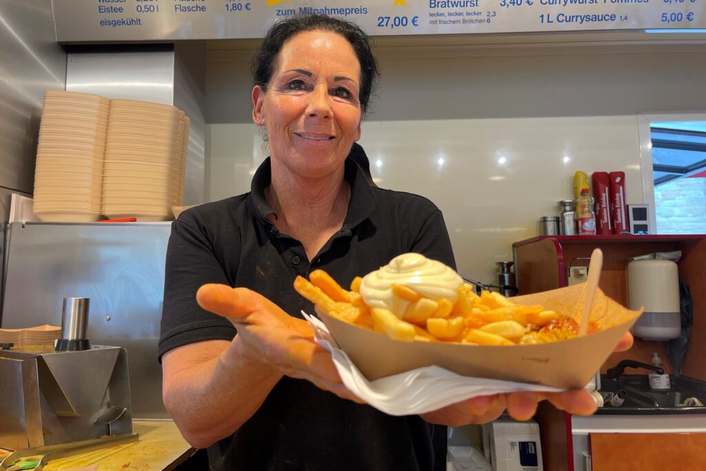 Eine Mitarbeiterin von Wurst Willi in Dortmund hält eine Schale mit Currywurst, Pommes und Mayo. Eine Mitarbeiterin von Wurst Willi in Dortmund hält eine Schale mit Currywurst, Pommes und Mayo.