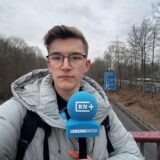 RN-Reporter Julius Obhues steht mit einem Mikrofon auf einer Brücke der A45. Unter ihm fahren Autos entlang.