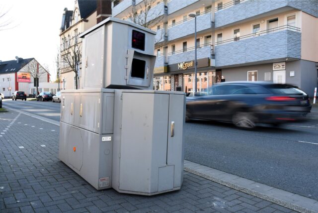 Ein Panzerblitzer der Stadt Herten steht an der Feldstraße in Herten, ein Auto fährt in diesem Moment etwas schneller vorbei.