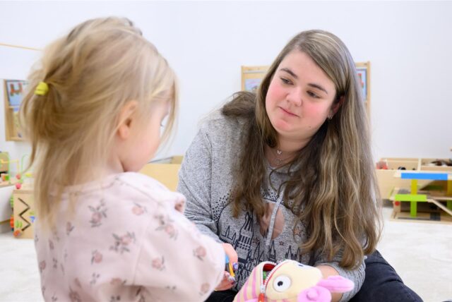 Eine Erzieherin mit einem Kind in einer Kindergartengruppe.