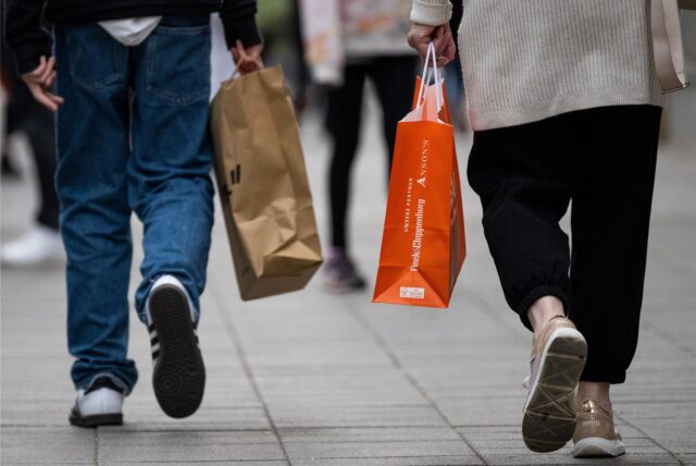 Menschen mit Einkaufstaschen gehen an einem verkaufsoffenen Sonntag in einer Fußgängerzone in NRW shoppen.