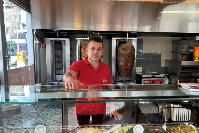Ein Mann in rotem Poloshirt steht im Dönerimbiss Orient Grill in Oer-Erkenschwick hinter der Theke und hat eine Hand auf den Tresen gelegt.