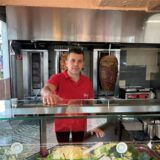 Ein Mann in rotem Poloshirt steht im Dönerimbiss Orient Grill in Oer-Erkenschwick hinter der Theke und hat eine Hand auf den Tresen gelegt.